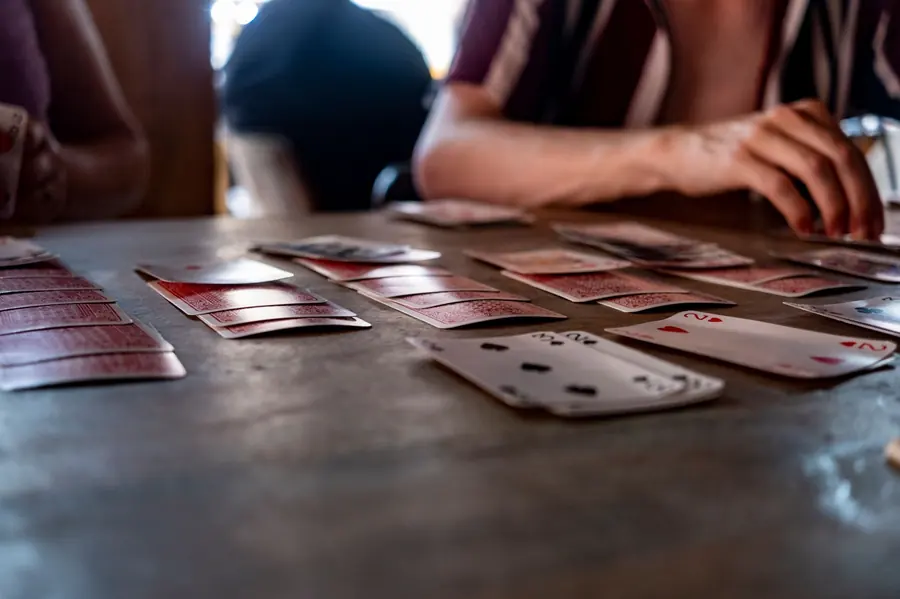 Playing cards laid out on a table with two people's hands visible above them