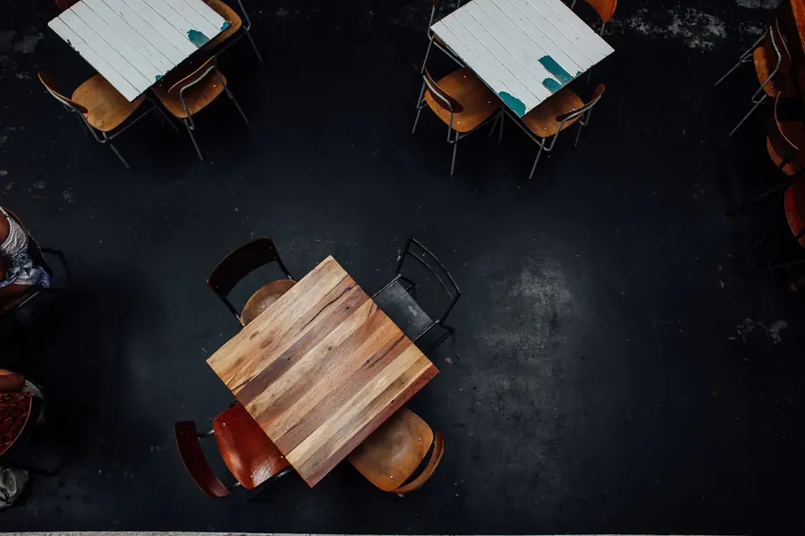 Overhead view of empty wooden tables and chairs on a dark restaurant floor