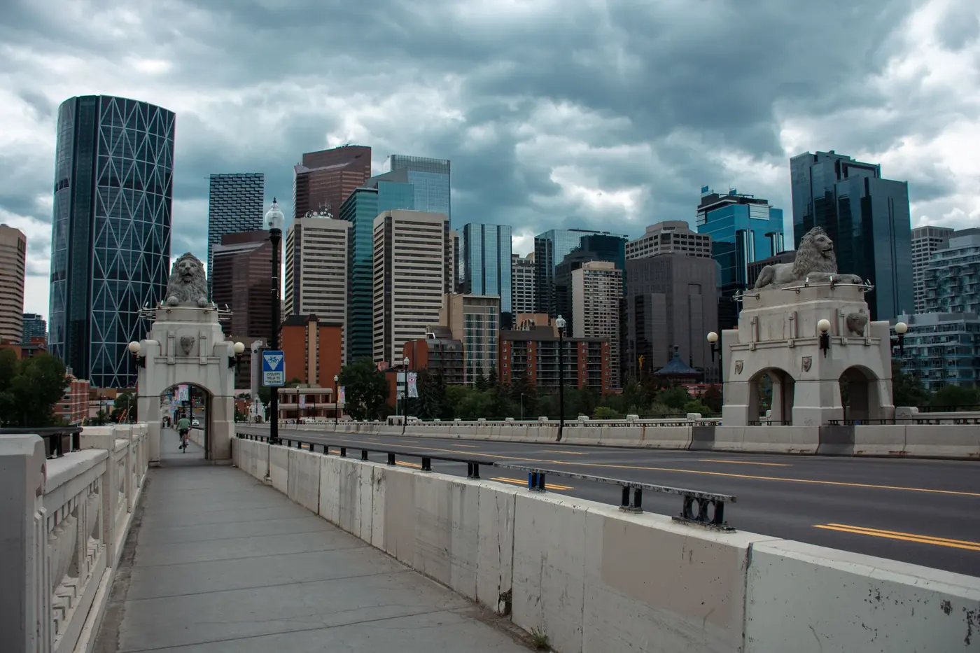 Calgary's downtown towers seen from the Centre Street Bridge, with the bridge's stone lion statues in the foreground under heavy cloud