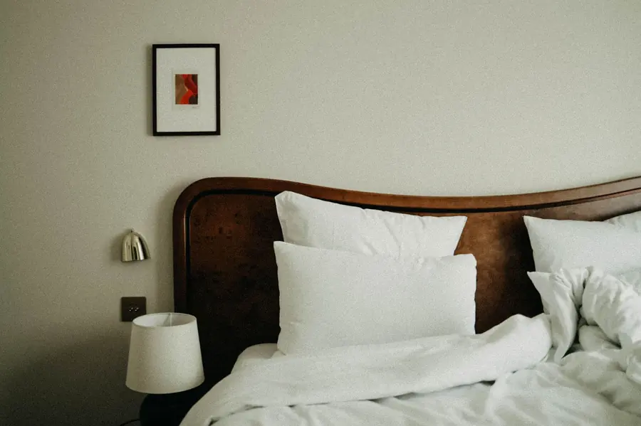 A made hotel bed with white linen, a dark wood headboard and a small framed print on the wall