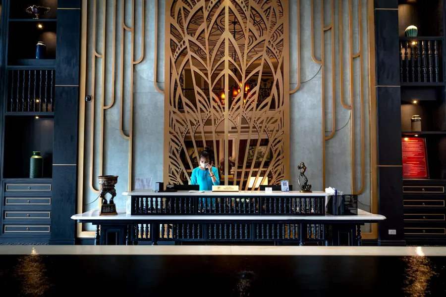 A dimly lit hotel reception desk with a decorative screen behind it and a receptionist on the telephone