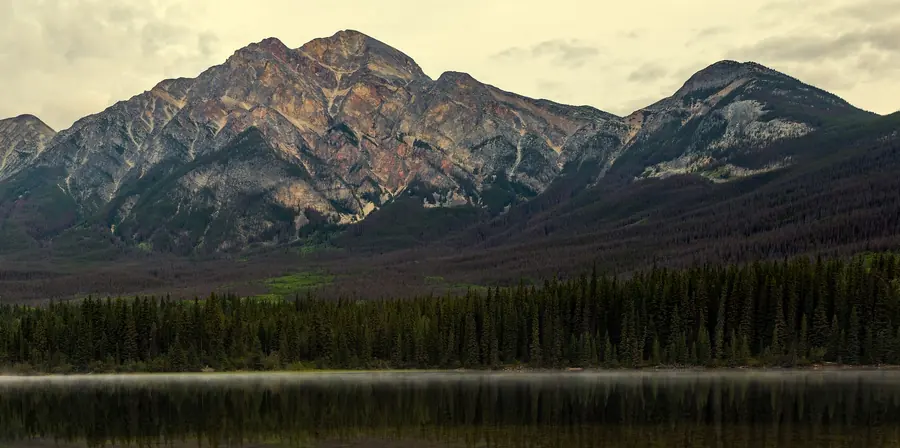 A rocky mountain ridge above a dark evergreen forest reflected in a still lake